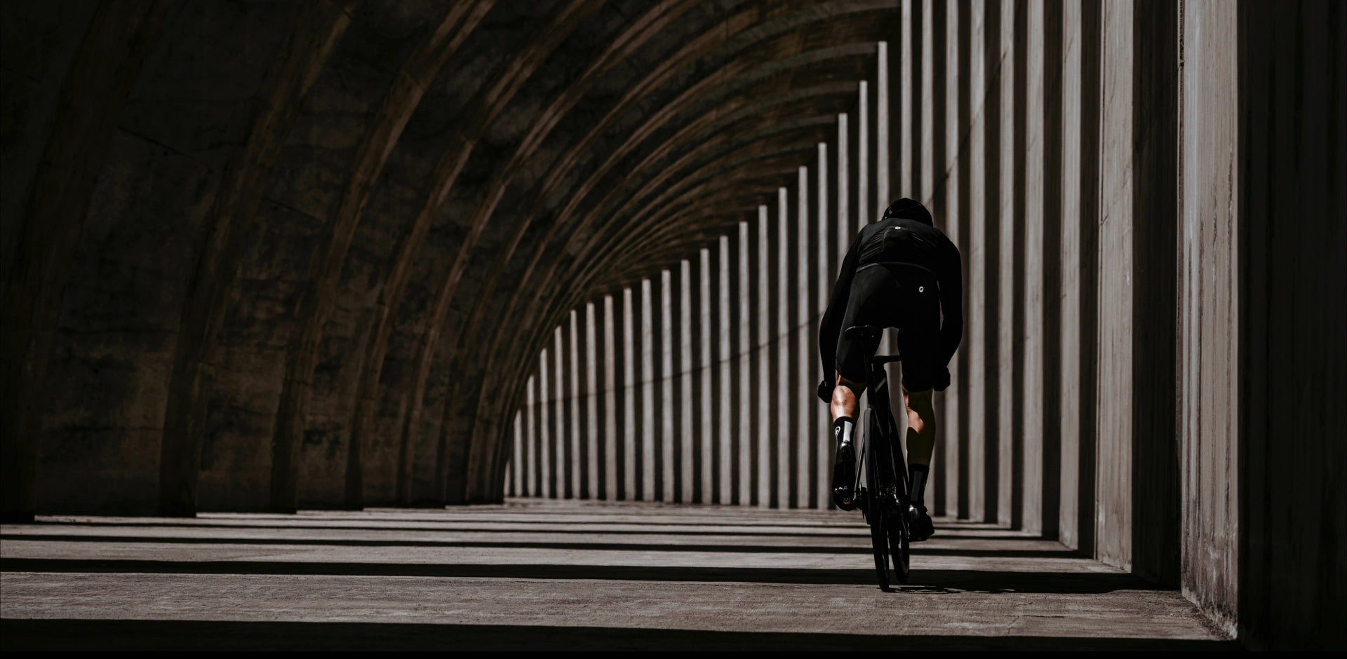 Lone cyclist in silhouette riding through an architectural corridor, embodying the essence of road biking @ Bici.